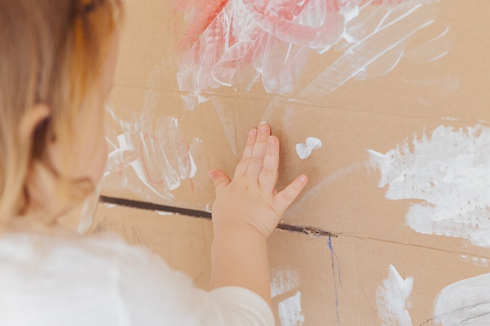 Ein Kind, das mit den Fingern auf Karton malt.