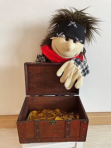 Tom der Pirat, eine Handpuppe mit einem schwarzen Kopftuch und einer Schatzkiste auf dem Arm