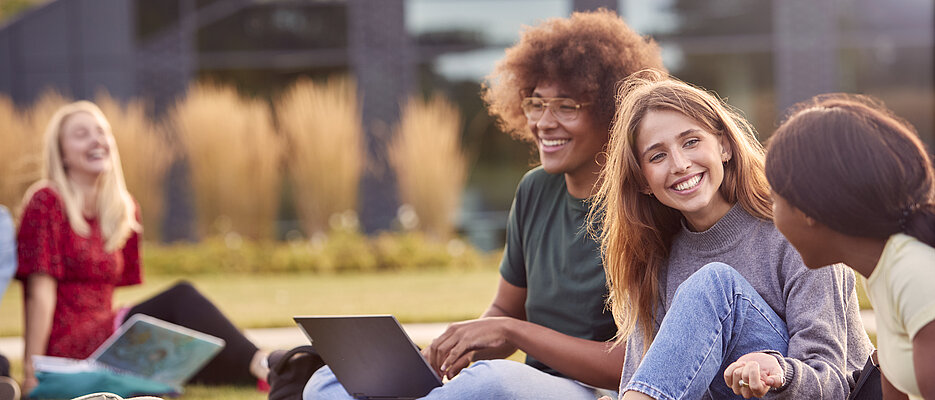 Group Of University Or College Students Sit On Grass Outdoors On Campus Talking And Working